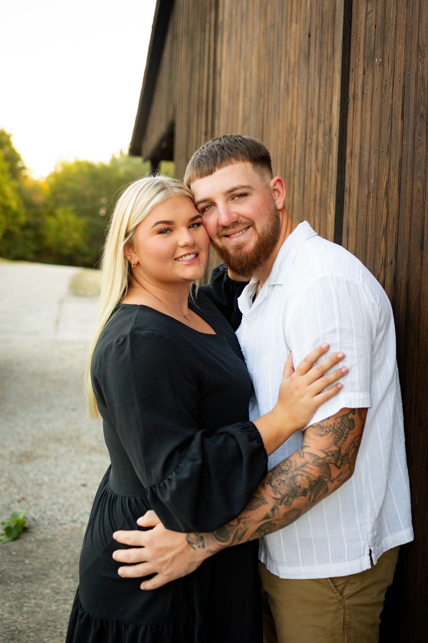 A couple embraces outdoors by a rustic wooden barn during golden hour.