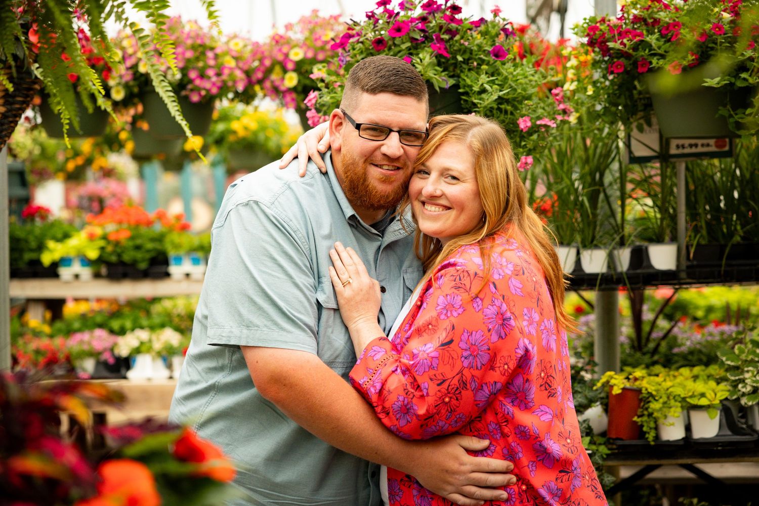 A couple laughs together surrounded by vibrant flowers and greenery in an outdoor garden setting.