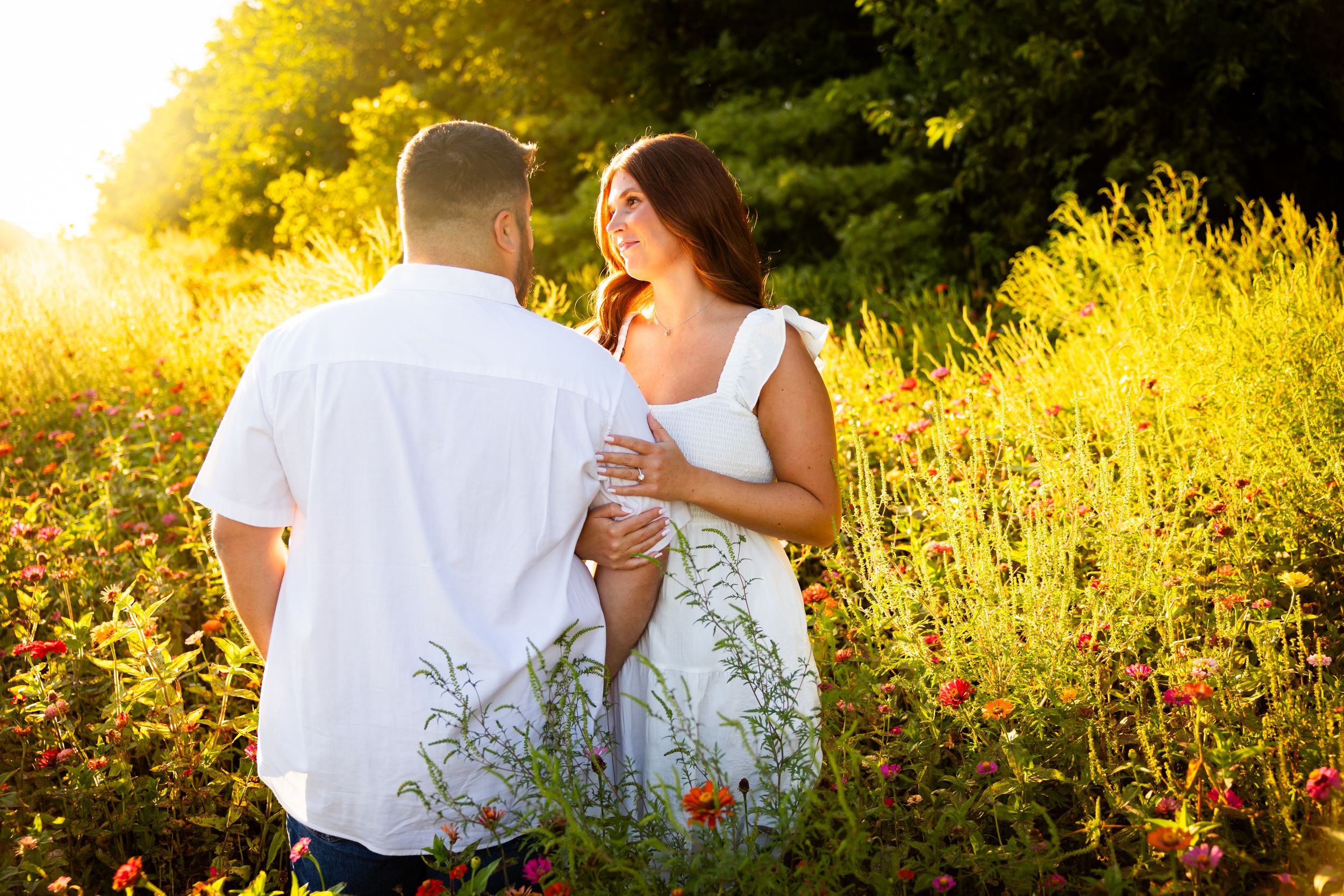 A romantic couple sits together in a golden wildflower meadow at sunset, creating a dreamy summer scene at Wolf Run Acres in Washington CH