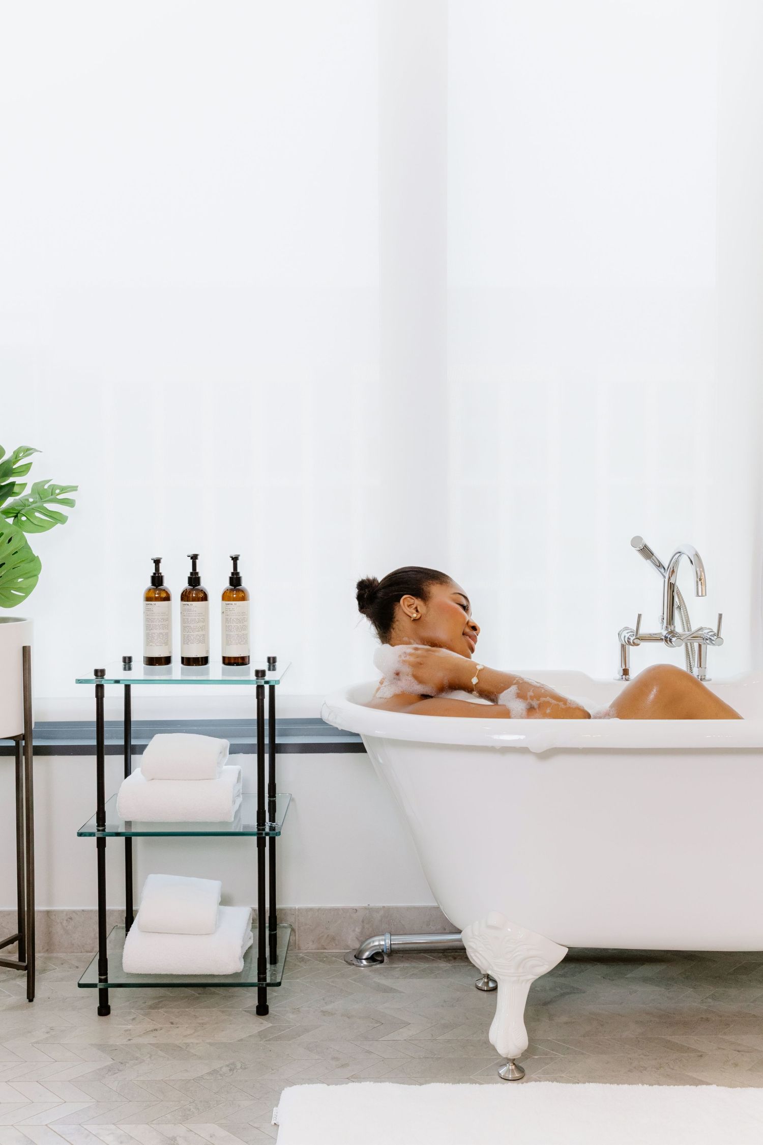 A relaxing spa setup with a clawfoot bathtub, black metal storage shelf holding essential oils and white towels.