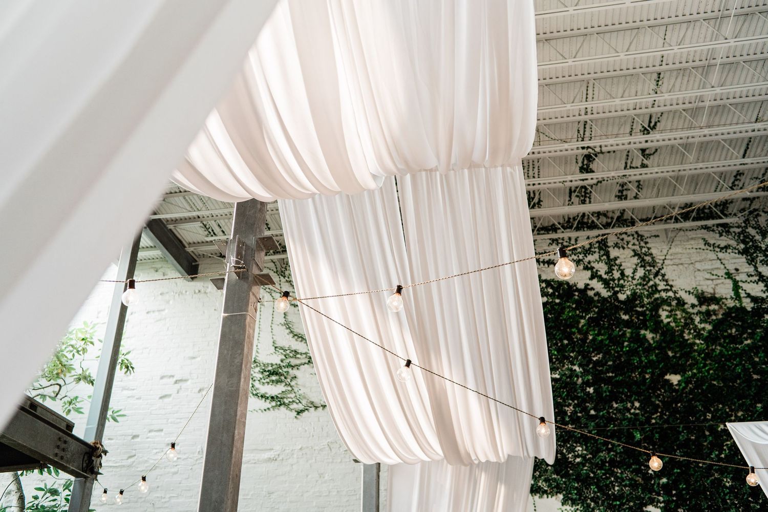 Elegant white fabric drapes cascade from an industrial ceiling, creating a romantic ceiling canopy for an event space.