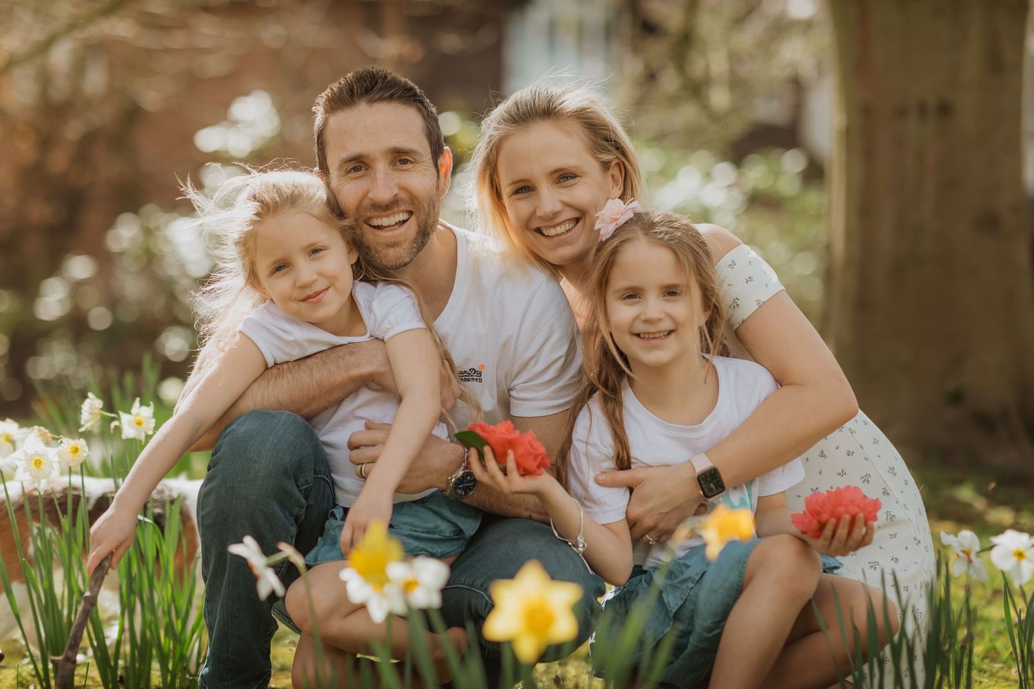 Happy family sits together in a blooming spring garden with yellow daisies and dandelions in the grass.