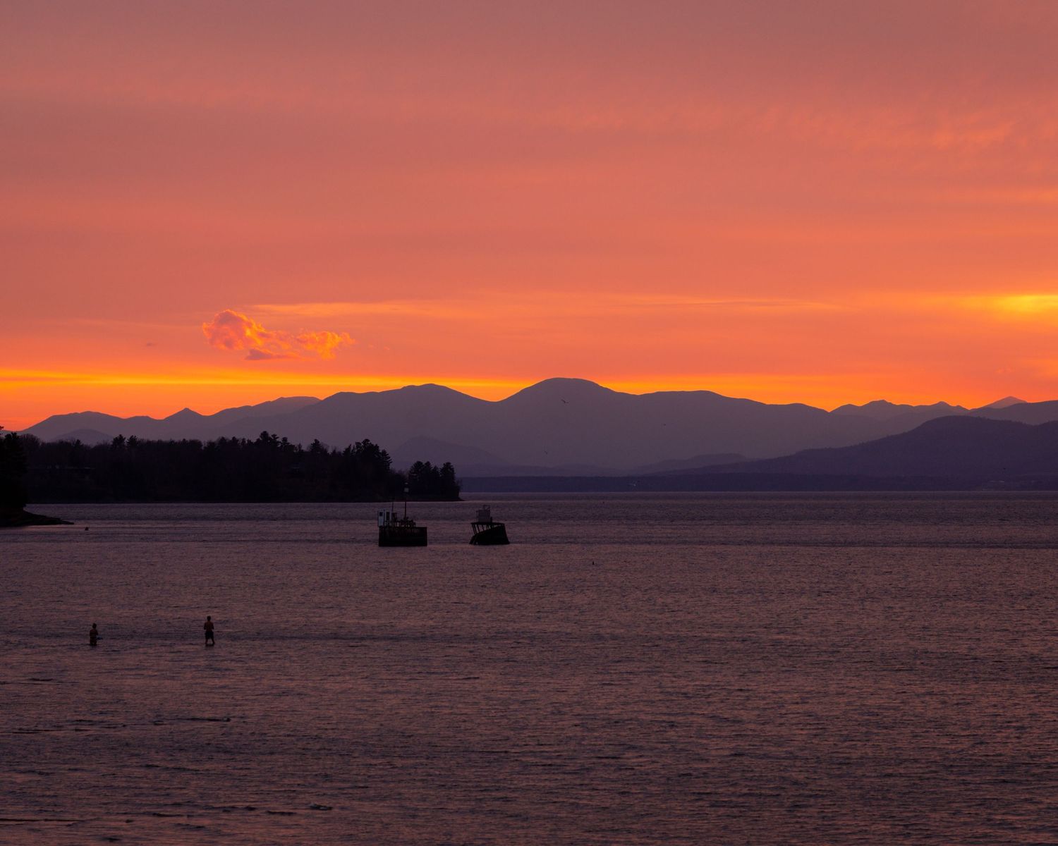 Orange sunset with people standing in Lake Champlain in Burlington, Vermont.