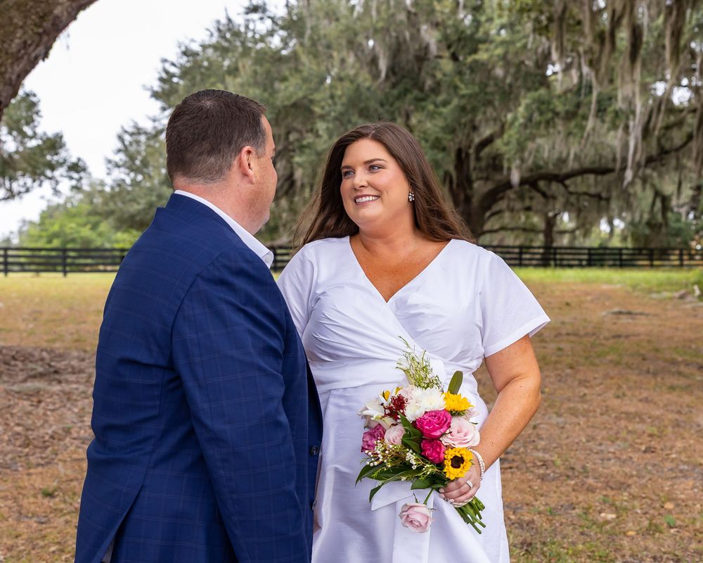 A couple poses together outdoors with a colorful bouquet on their wedding day.