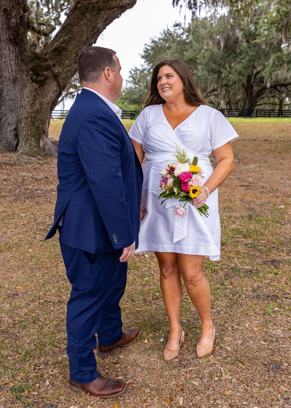 A couple poses playfully under oak trees during an outdoor photoshoot.