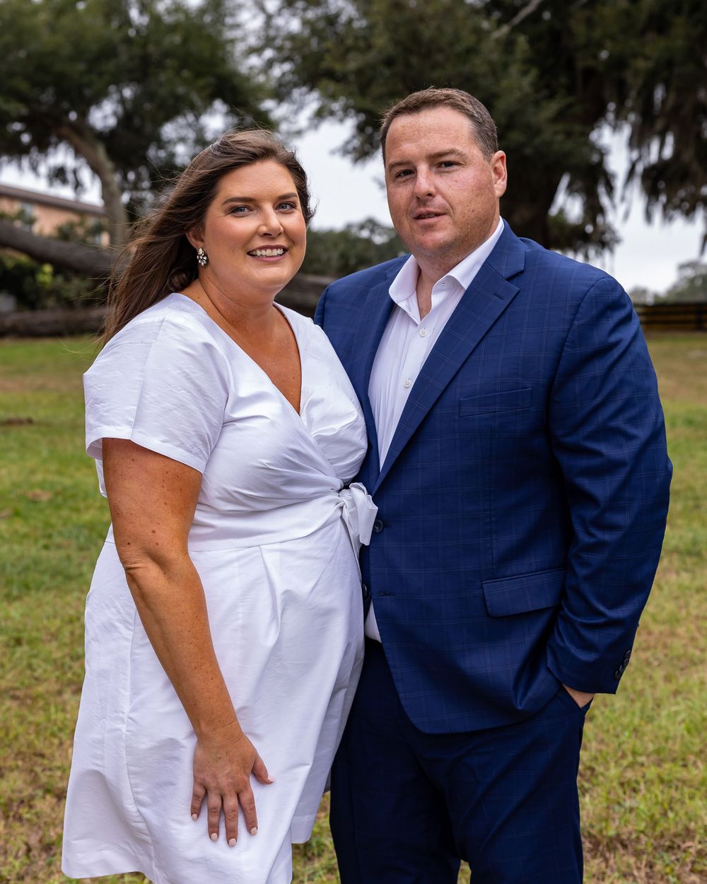 Couple in coordinating white and blue outfits pose together in a park setting.
