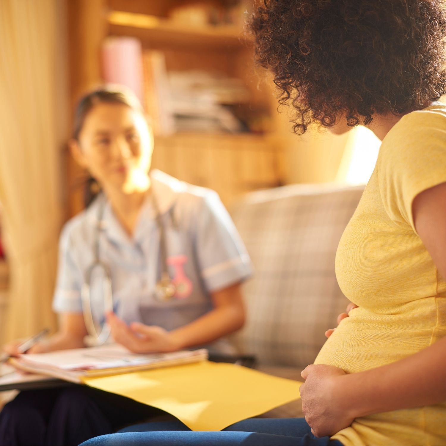 Healthcare worker meets with pregnant patient in yellow dress during prenatal checkup consultation.