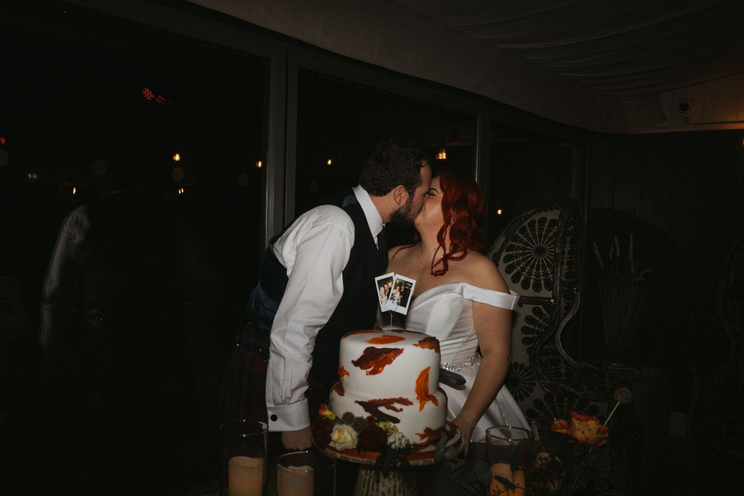Couple sharing an intimate moment next to their wedding cake in a dimly lit reception venue.