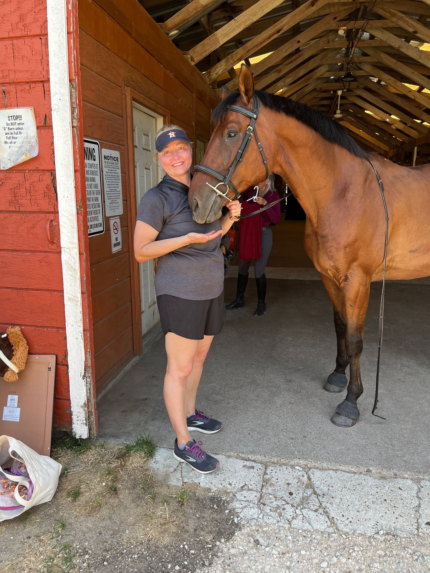 A bay horse stands in a stable aisle with a handler wearing shorts and a dark shirt in Alvin, Texas