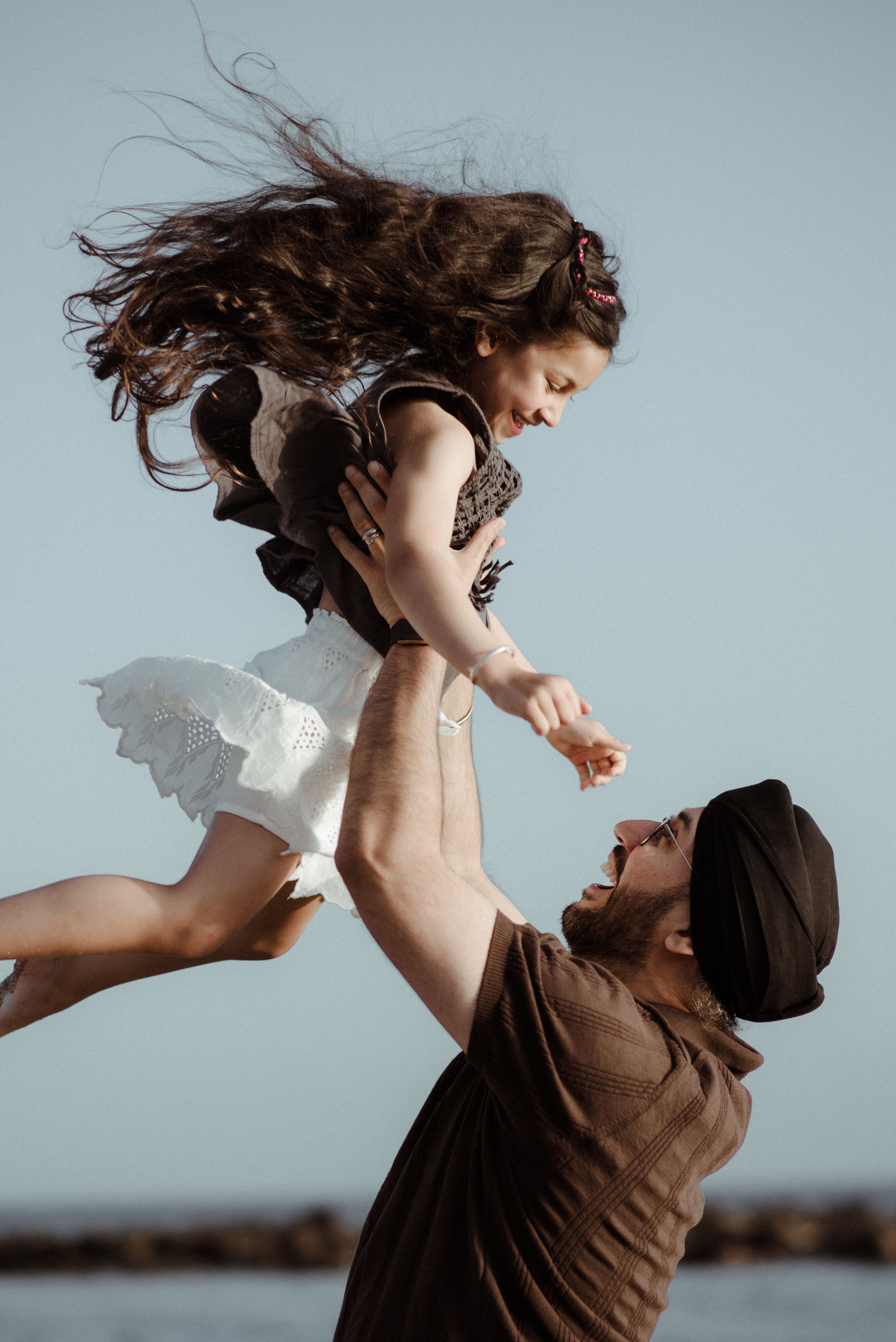 Dynamic outdoor portrait of daughter and dad sharing a joyful moment as one lifts the other high in the air at Playa del Duque.