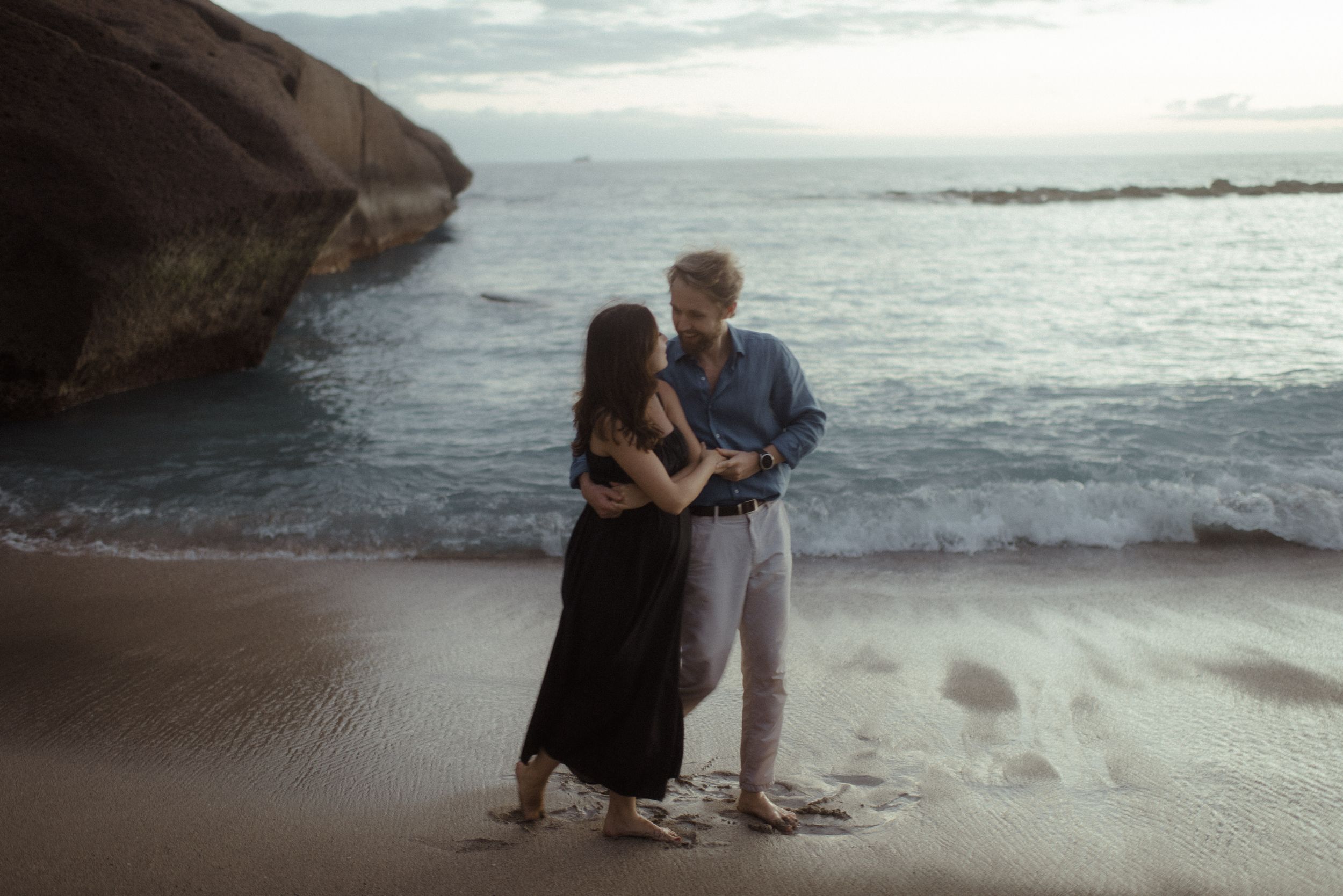 Romantic beach photoshoot featuring couple sitting near ocean caves during golden hour.