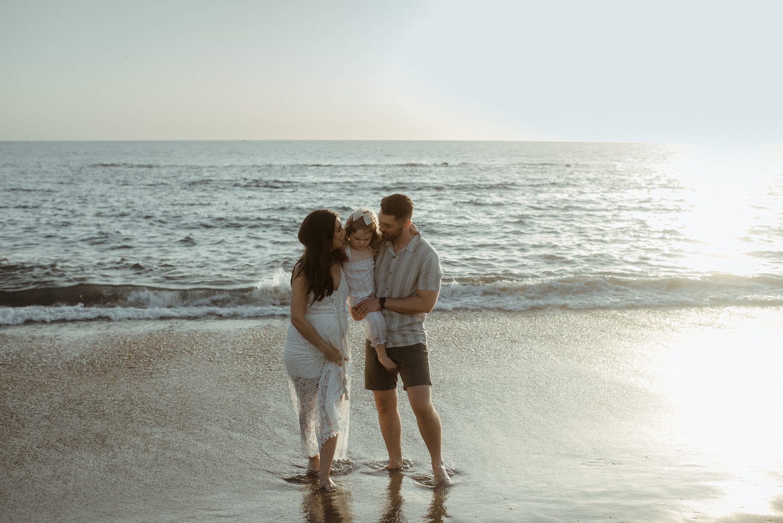 A couple holds hands while walking along a misty beach at sunset with the ocean waves in the background at Playa del Duque..
