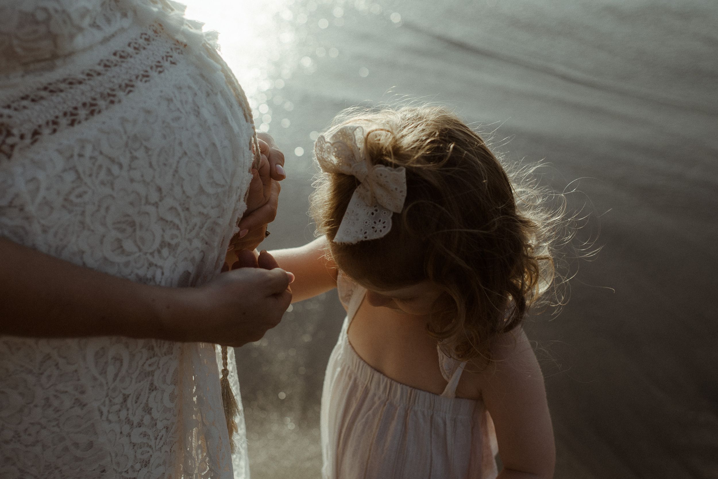 Tender moment captured in soft sunlight with white lace dress and flowing hair at Playa del Duque.