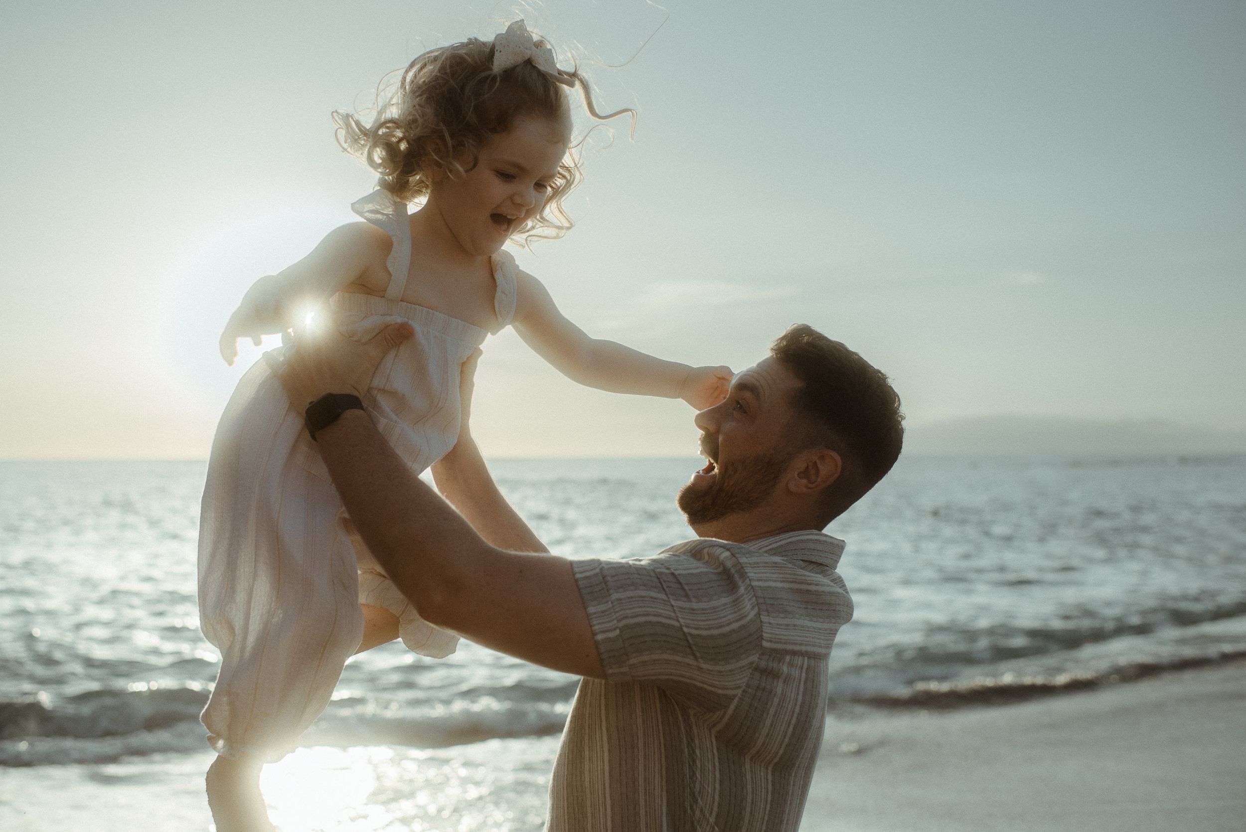 A couple sharing a joyful moment at the beach during sunset as waves crash behind them along the shore at Playa del Duque.
