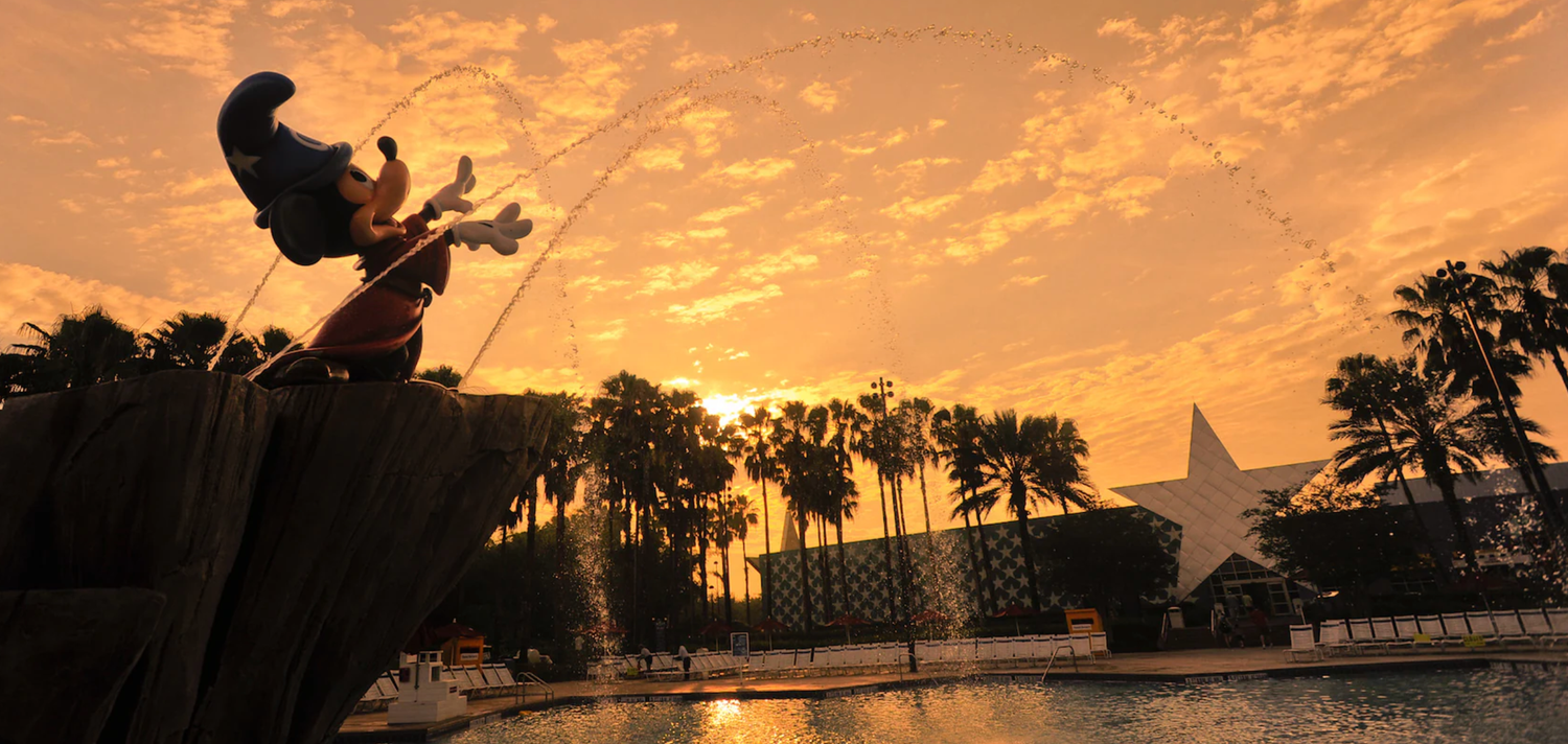 Silhouette of jumping figure against orange sunset sky with palm trees.