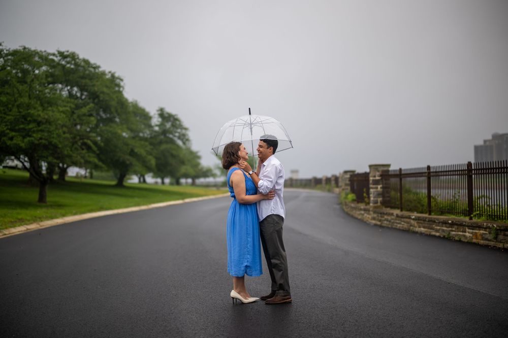 Two people share a romantic moment on a misty road surrounded by green trees and grass, in baltimore