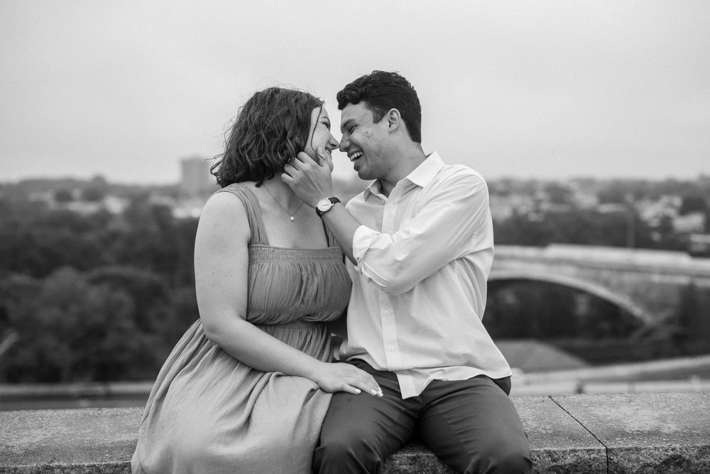 A romantic black and white portrait of a couple sharing a tender moment while sitting outdoors with a scenic overlook, in baltimore