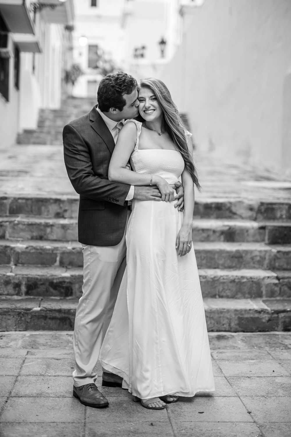 A romantic black and white wedding photo featuring a couple embracing on stone steps with classic attire.
