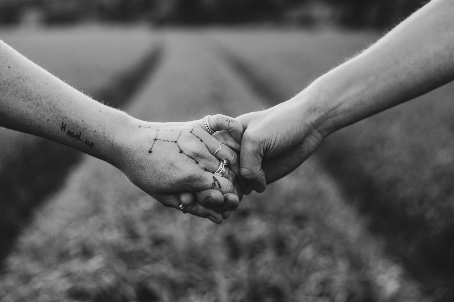 A black and white photo of two hands reaching to hold each other with a constellation tattoo on one hand in nature.