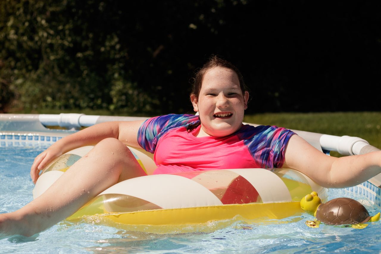 Girl sitting in yellow pool float swimming in the sun - lifestyle family photographer in South Lyon, Michigan.