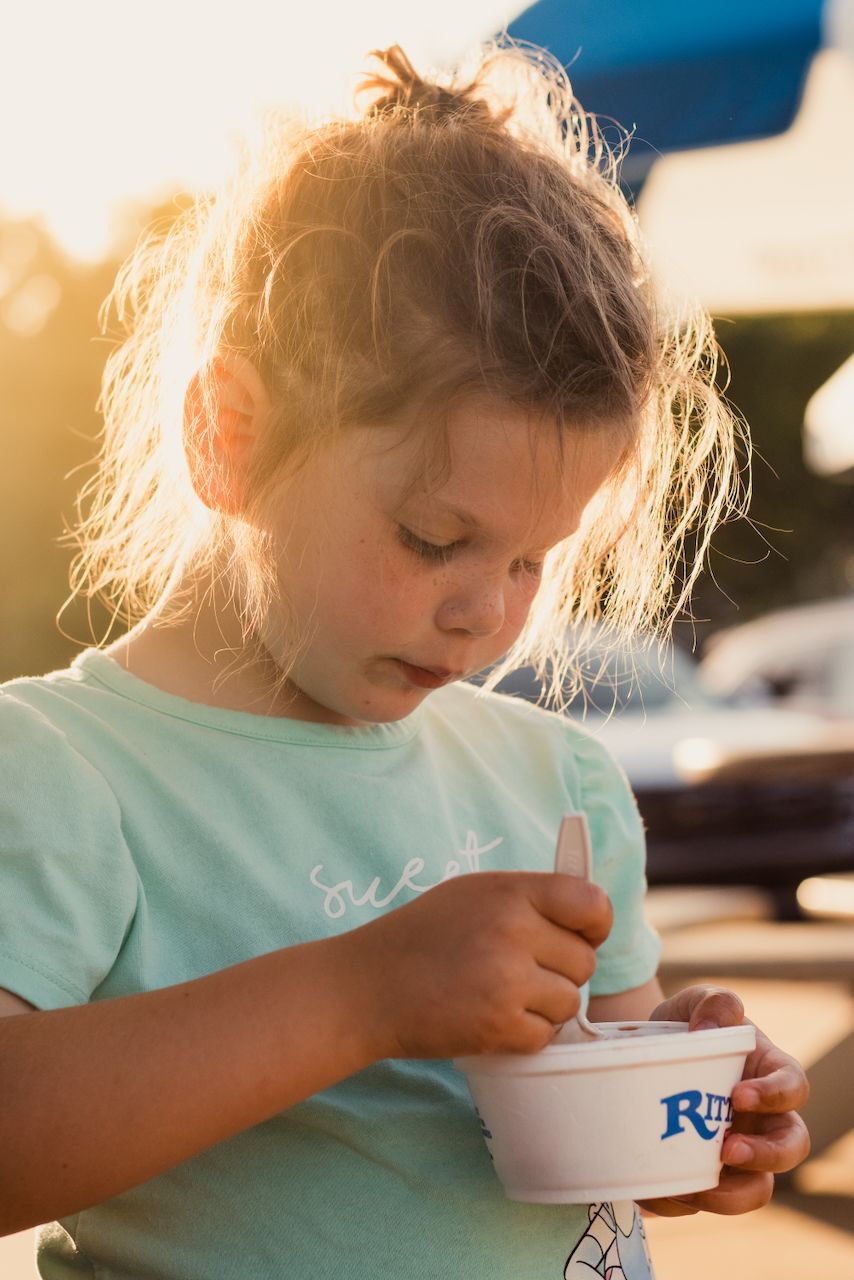 Little girl eating ice cream with sprinkles in the golden sun - lifestyle family photographer near Brighton, Michigan.