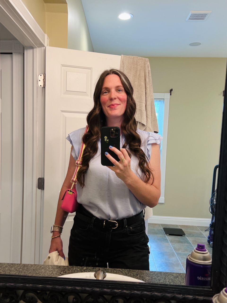 Brunette woman takes mirror selfie wearing white top, black jeans, and pink crossbody bag.