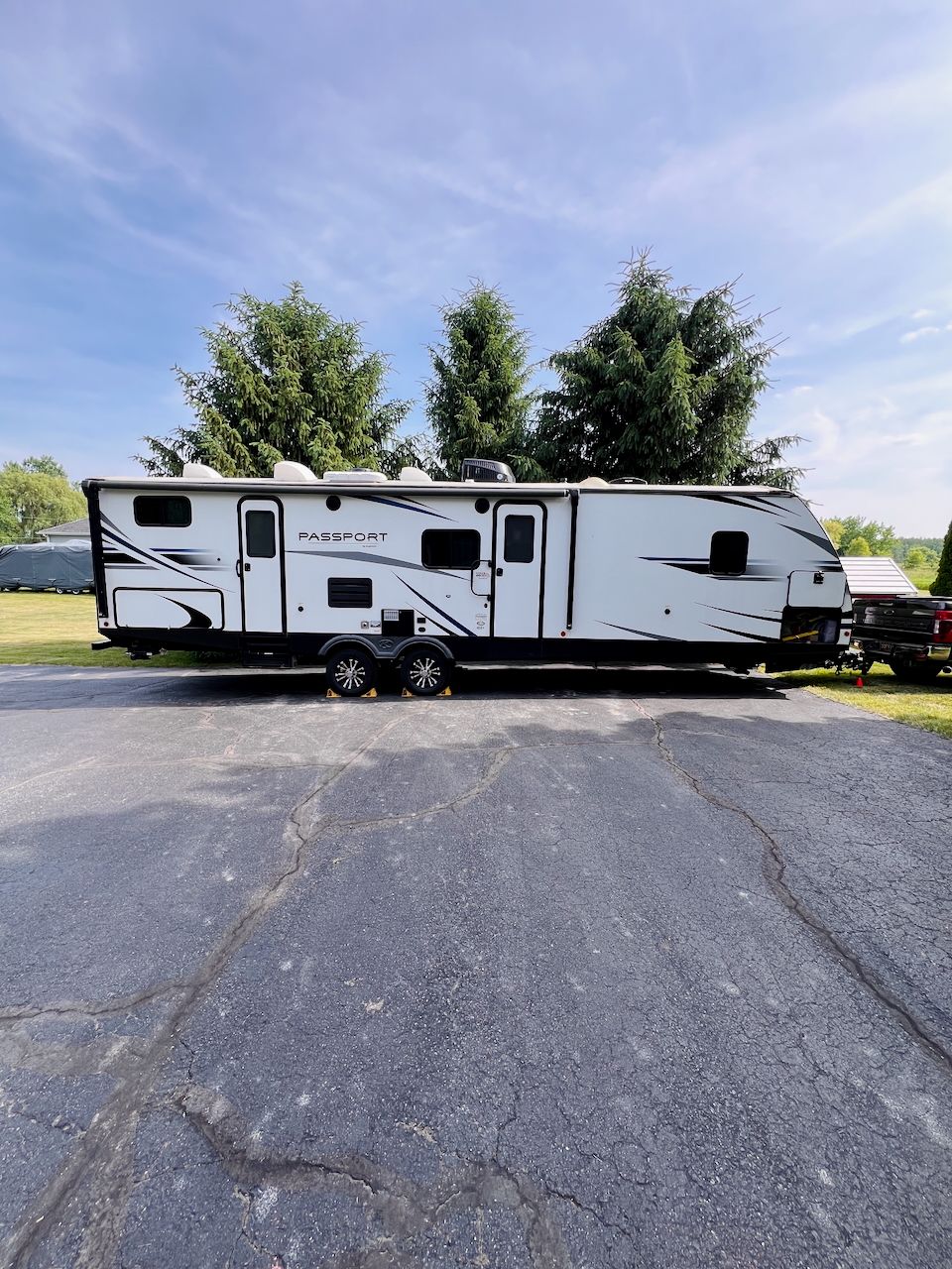 Large Passport travel trailer RV parked in a lot under a partly cloudy blue sky.