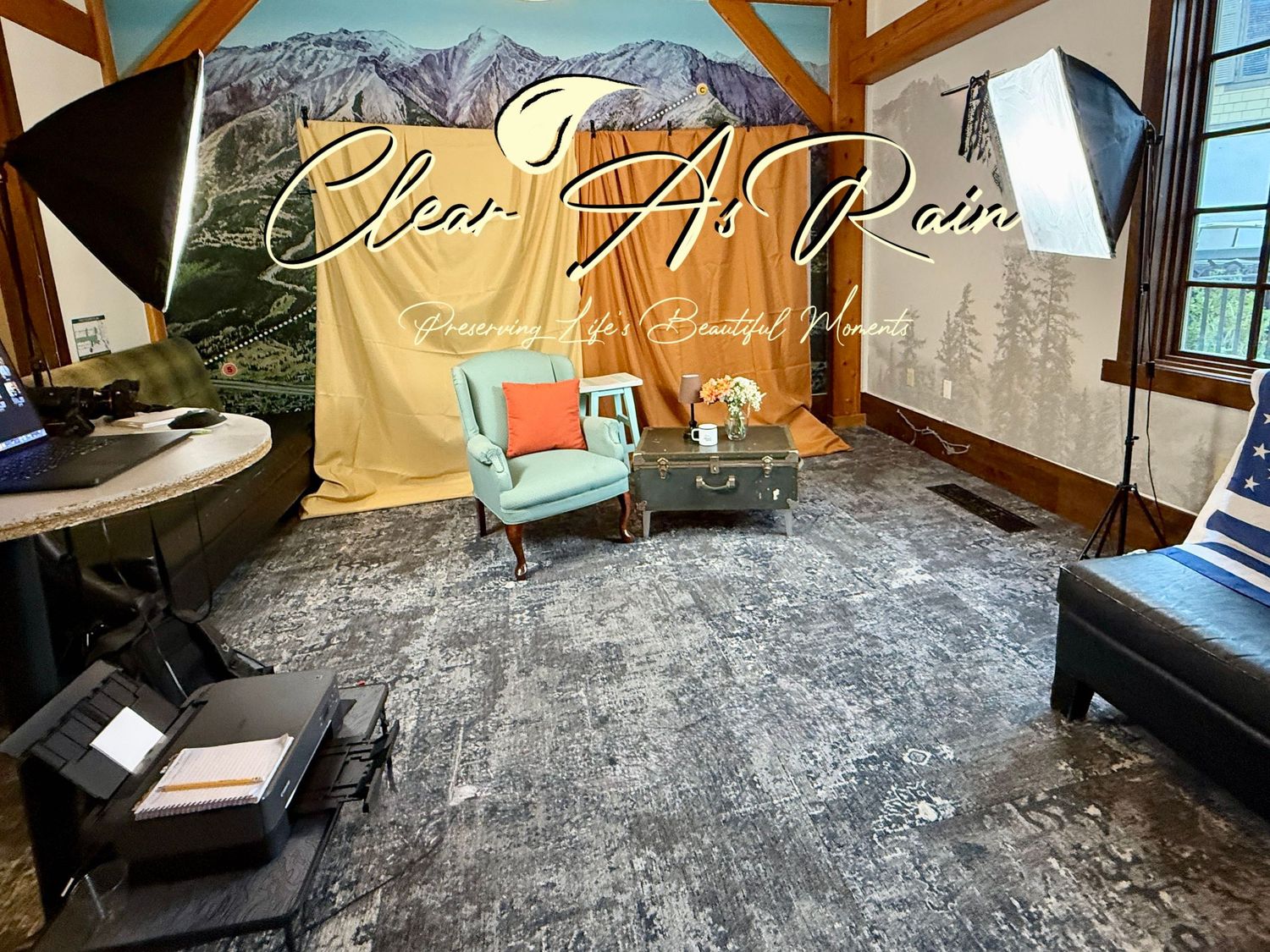 The ultimate photobooth experience with mint chair, backdrop, and mountain views through windows in rustic wooden room.