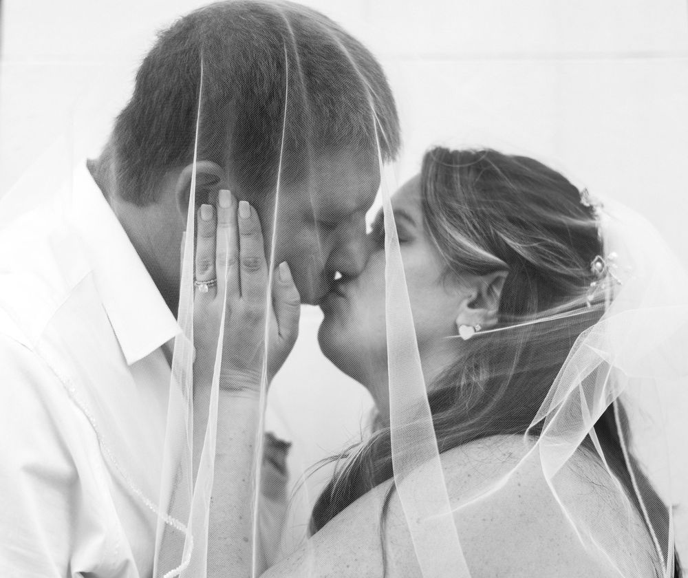 A romantic black and white wedding photo showing a tender moment between a couple with bridal veil.