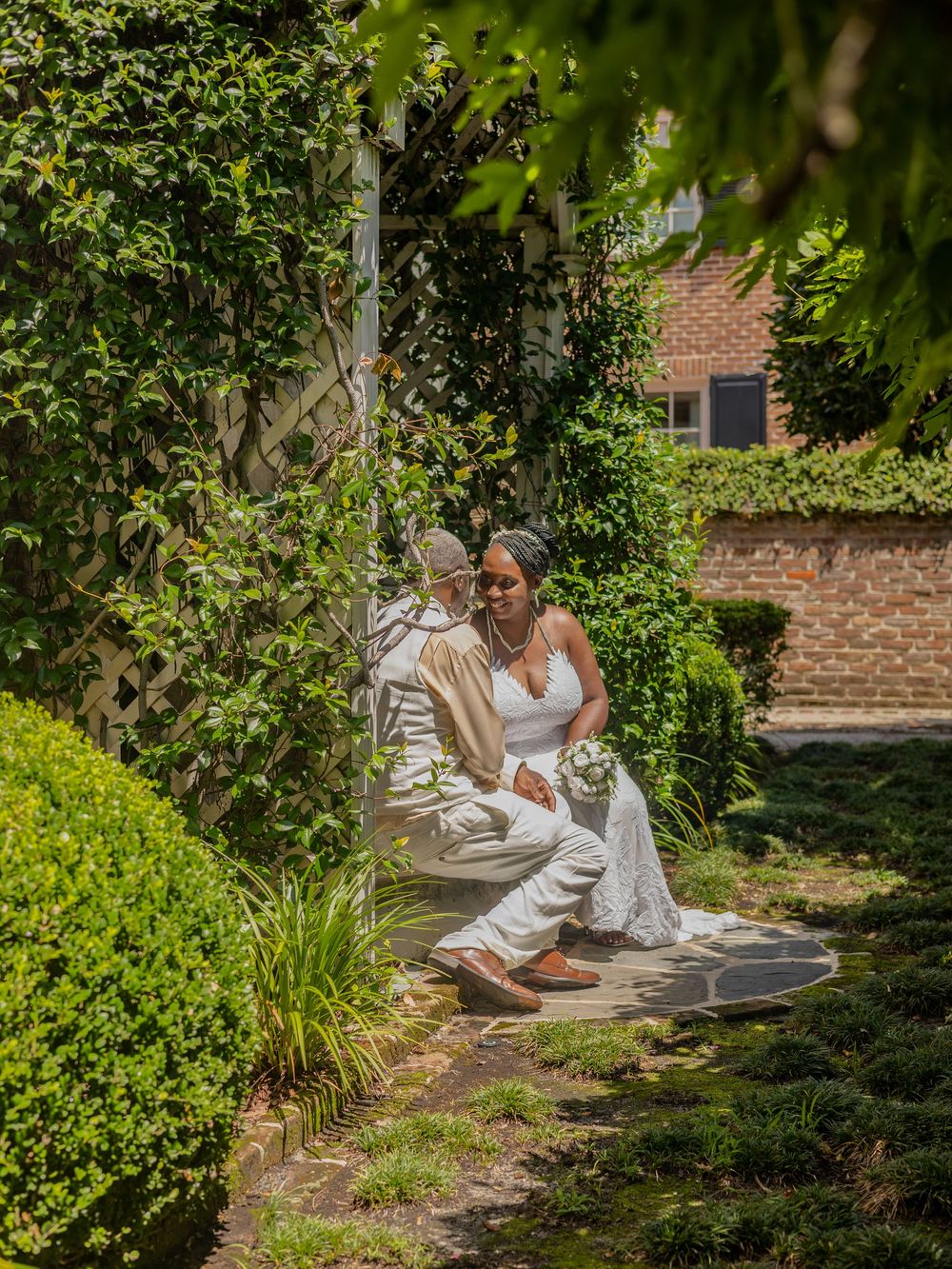 Artistic wedding photography in a lush garden setting with white-clad figures posed among greenery.