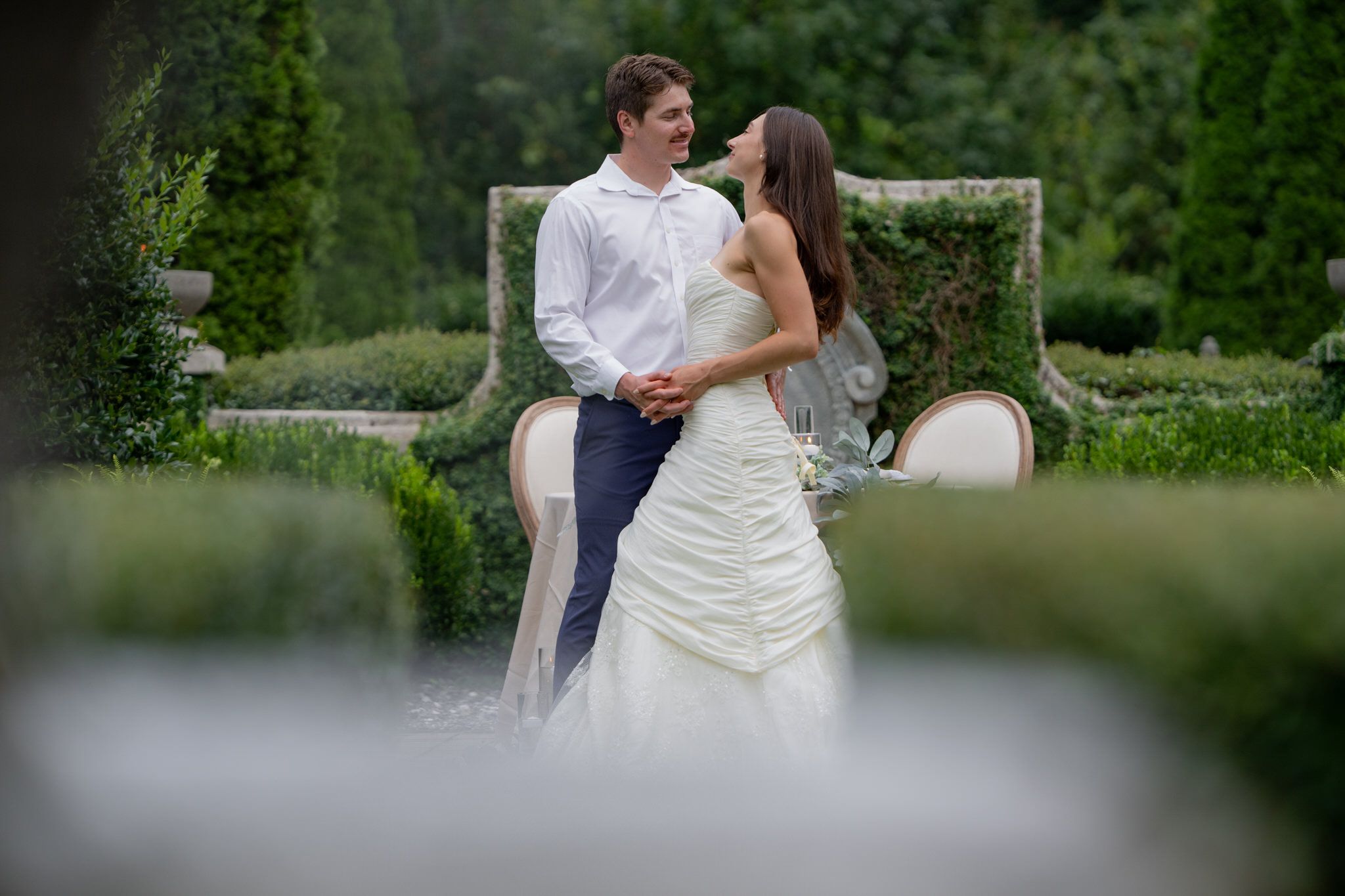 A couple shares a romantic moment outdoors in a garden setting during a wedding celebration.
