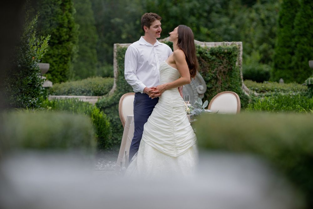 A couple shares a romantic moment outdoors in a garden setting during a wedding celebration.