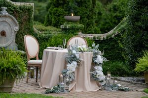Elegant wedding ceremony setup with blush pink chairs and eucalyptus garland decorations in an outdoor garden setting.