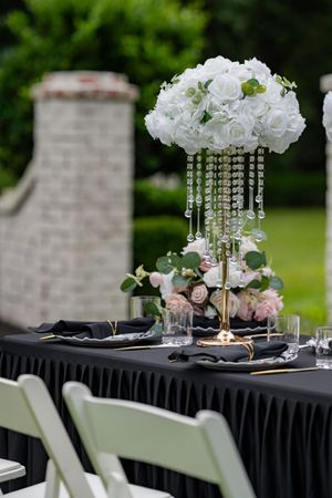 Elegant outdoor wedding table settings with crystal candelabras and white floral centerpieces on black tablecloths.