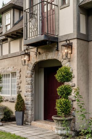 Elegant stone and stucco townhouse entrance with wrought iron lanterns, burgundy doors, and manicured topiaries.