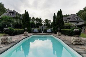 Panoramic view of a luxurious backyard swimming pool with stone pillars and lush greenery surrounding the area.