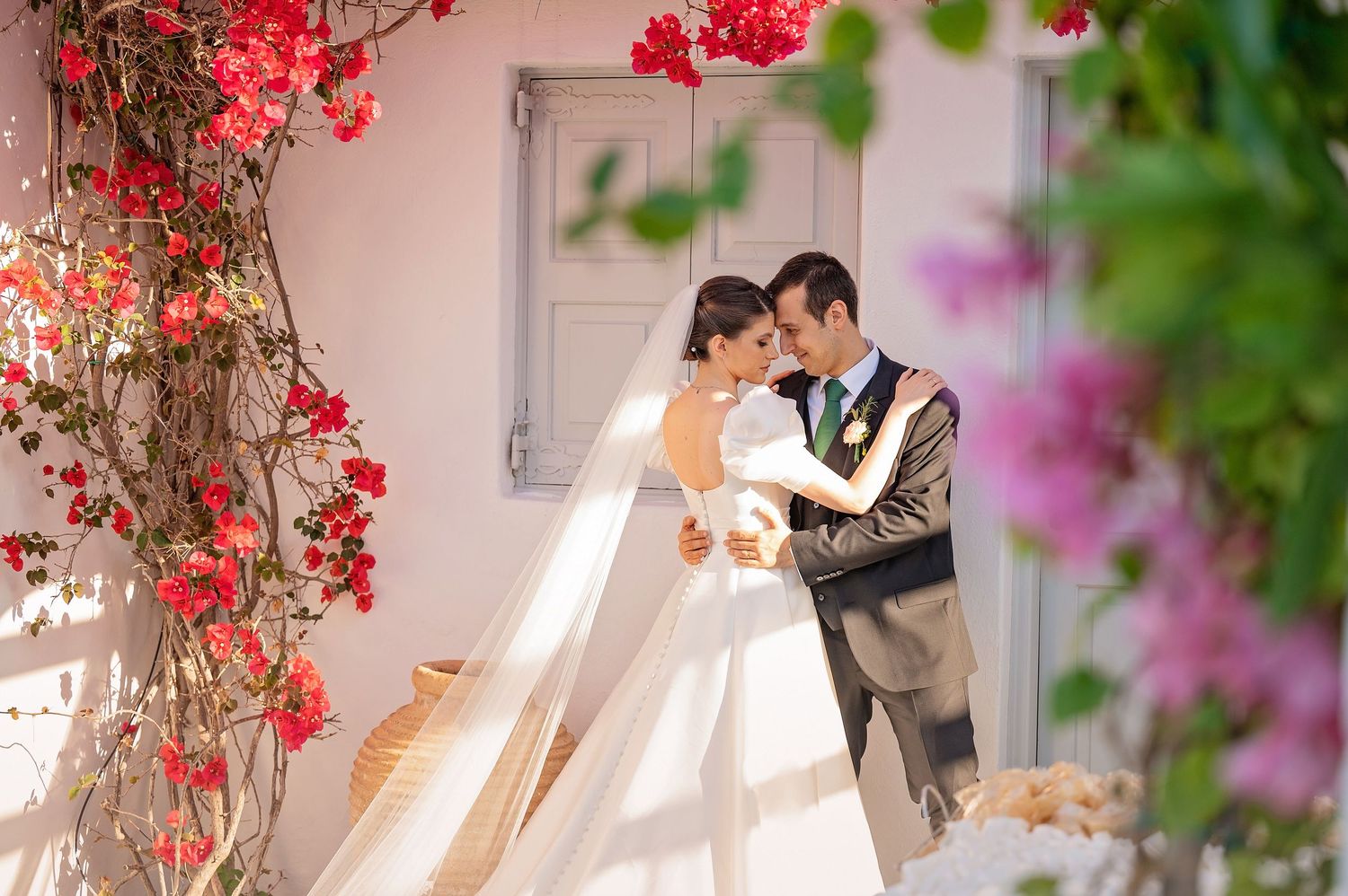 A couple shares an intimate moment among red flowers and greenery.