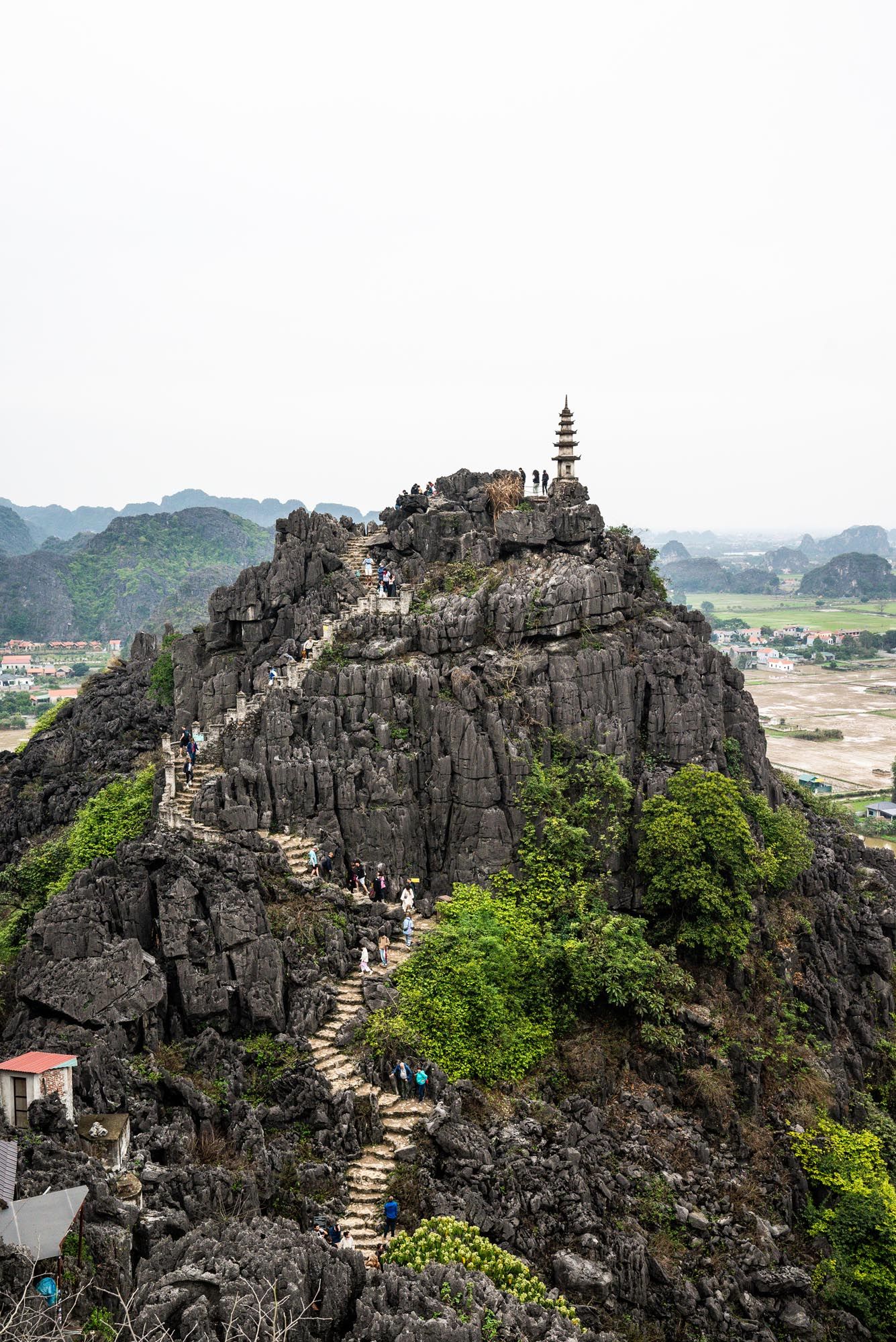 Ancient pagoda temple perches atop a dramatic limestone peak with stone steps winding up the mountainside in Ninh Binh, Vietnam.
