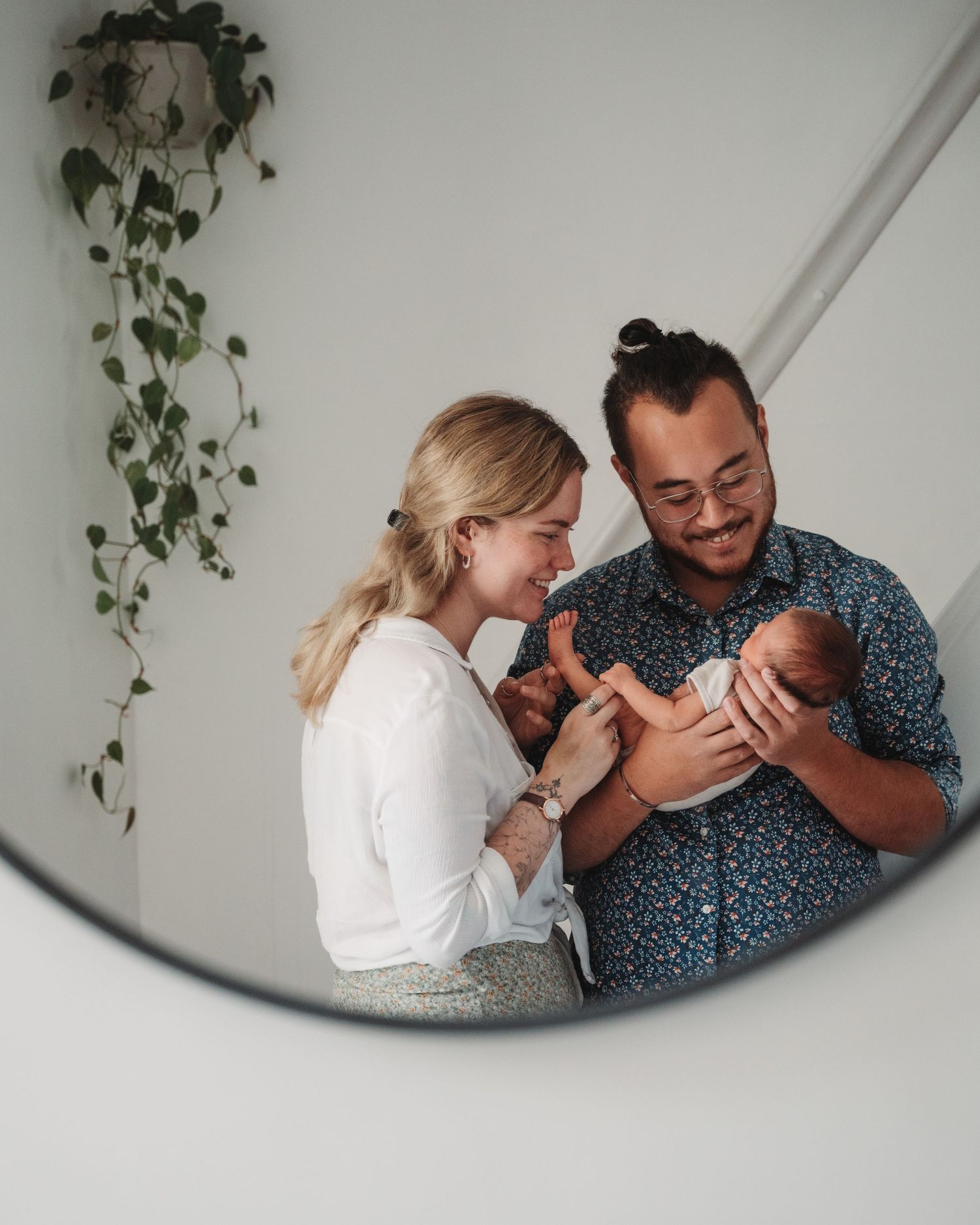Parents looking lovingly at their newborn baby through a circular mirror reflection.