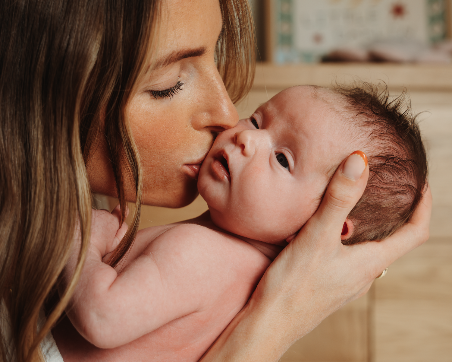 Mother tenderly kissing her sleeping newborn baby in an intimate close-up portrait.