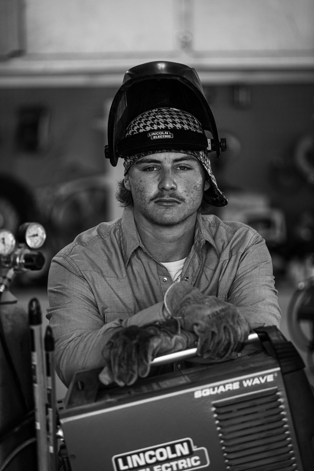 A welder in protective gear operates a Lincoln Electric welding machine in a workshop.
