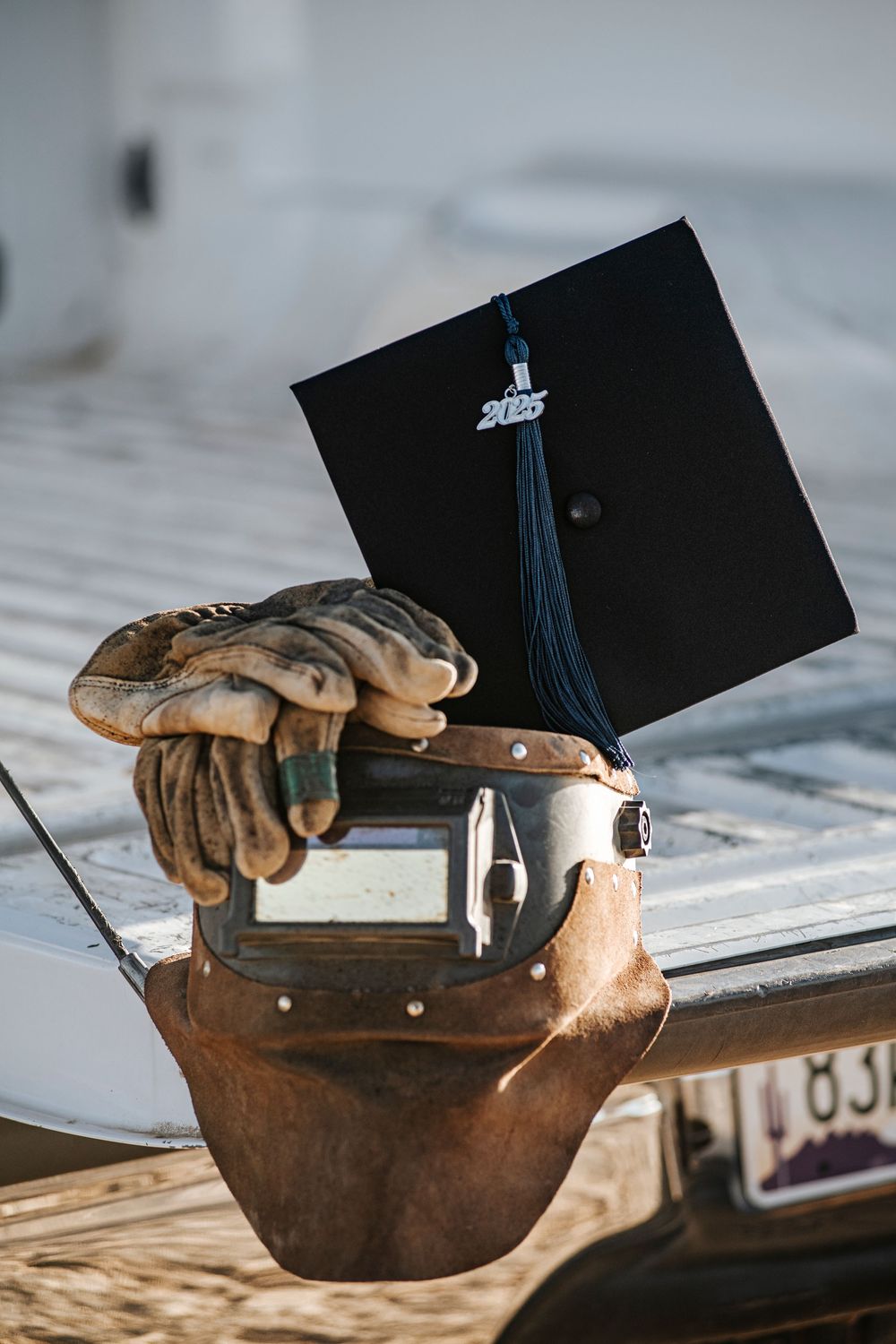Graduation cap and work gloves placed on welding equipment in bright sunlight.