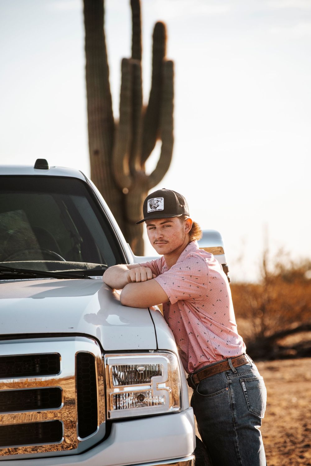 A silver Ford truck parked beside a tall saguaro cactus in the Arizona desert at sunset.