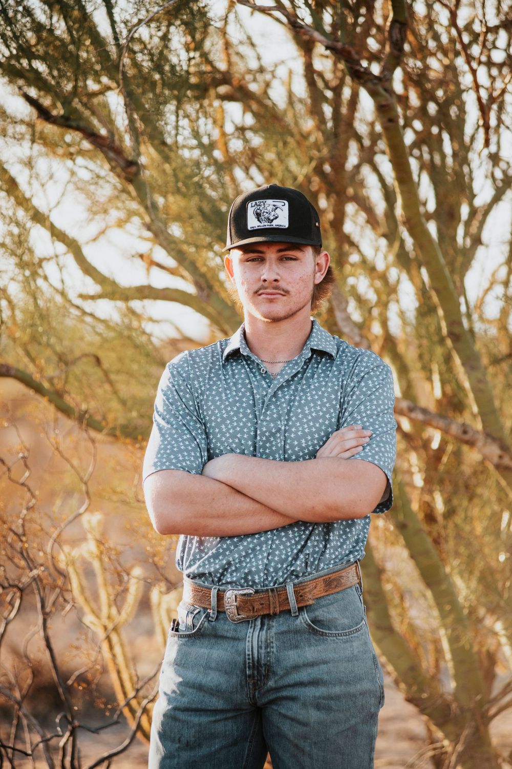 Casual portrait of a person in a western hat and patterned shirt against a rustic desert backdrop.