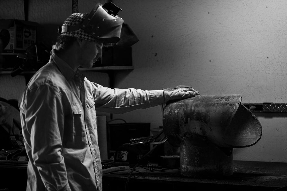 A welder wearing protective equipment works in dim lighting on a metal fabrication project.