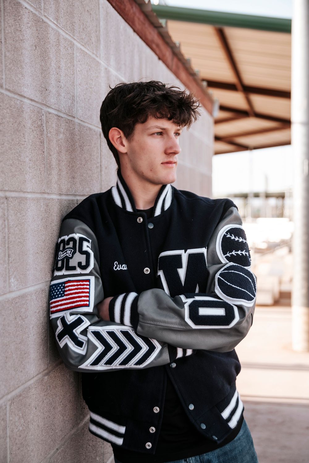 Varsity letterman jacket with American flag patch and graphics displayed against concrete wall.