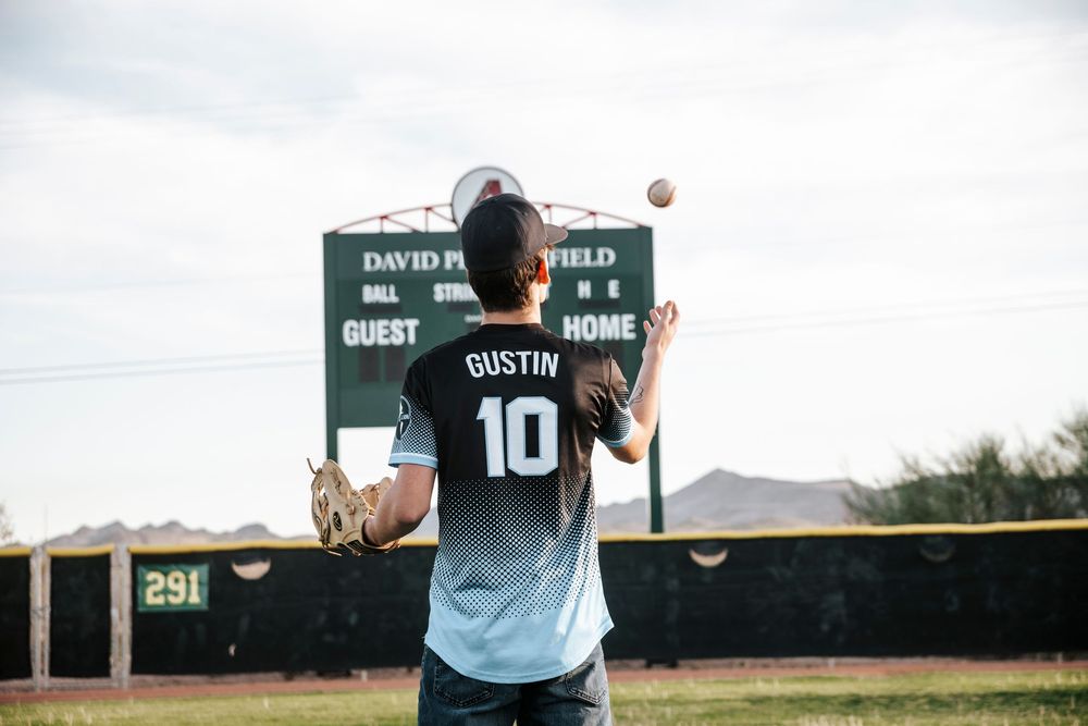 Player adjusts baseball scoreboard numbers during game at outdoor field.