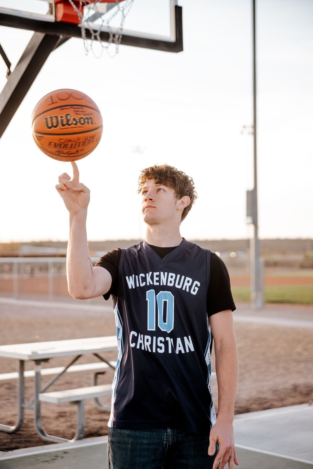 Player in Wickenburg Christian jersey spins basketball on finger on outdoor court.
