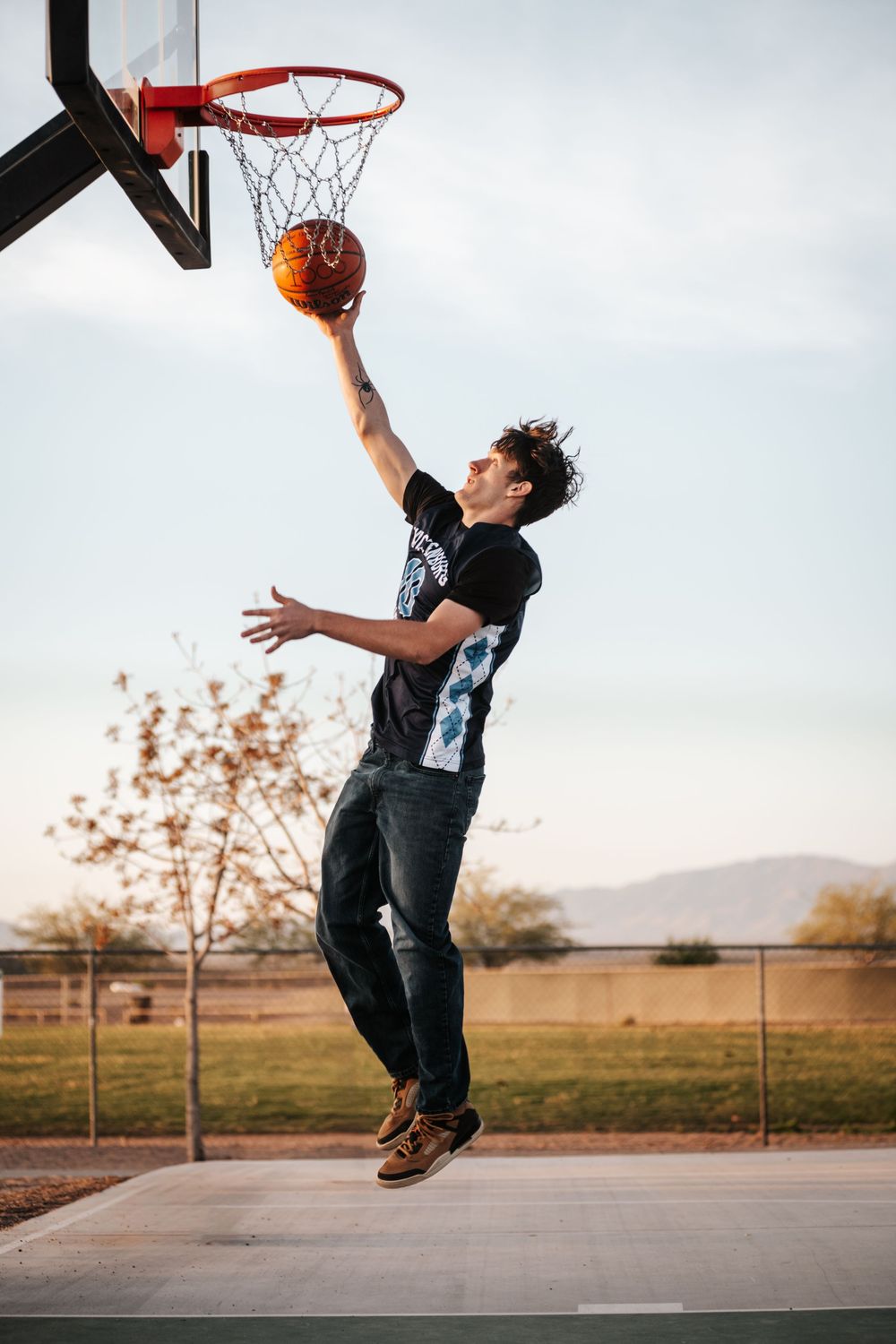 Basketball player in dark jersey leaps for layup on outdoor court.