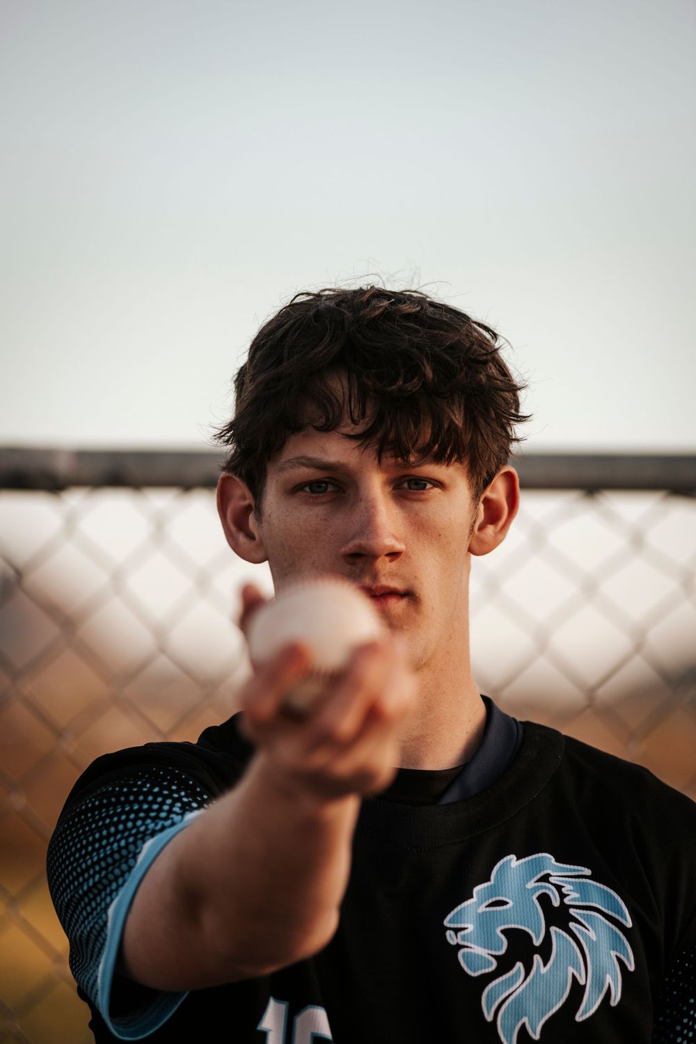 Player holds baseball while wearing dark athletic jersey with blue lion logo.